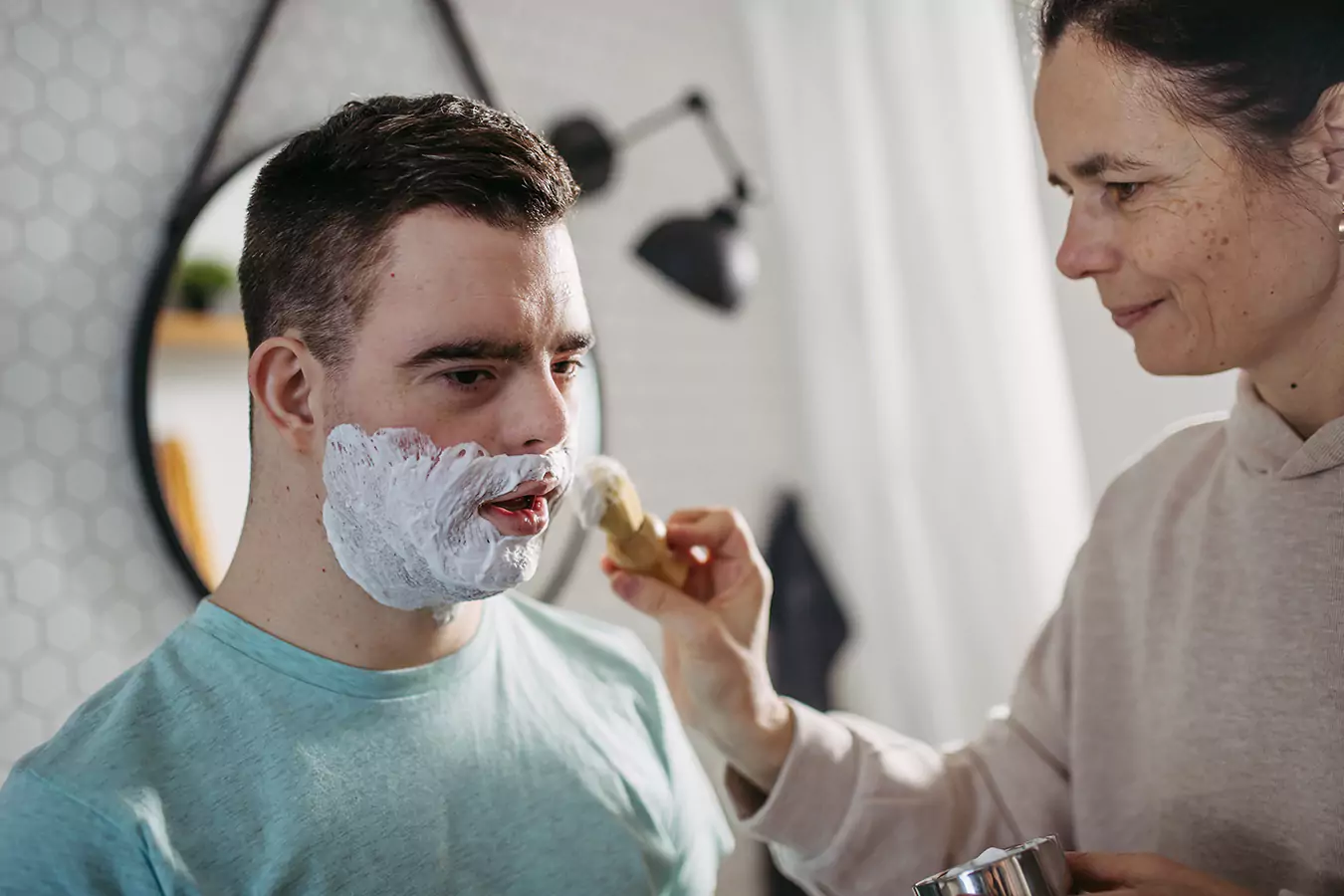 A disabled man and his support worker helping him shave his beard